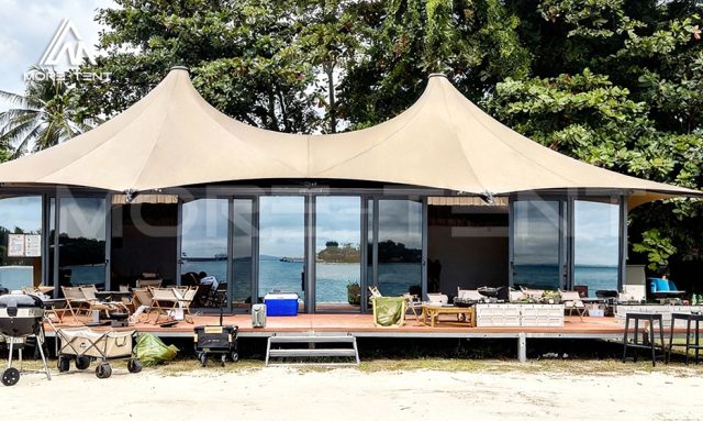 Hexagonal double-peak lounge tent with panoramic glass walls facing the sea