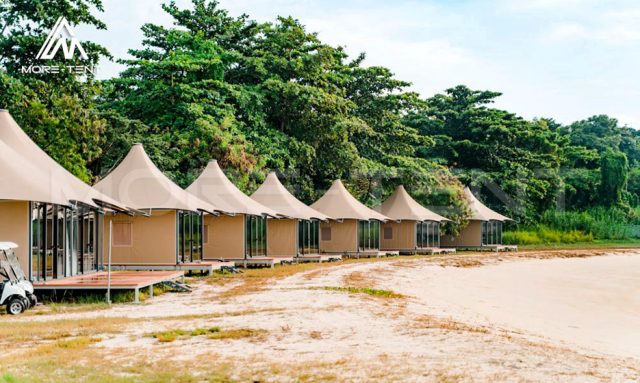 Quadrilateral safari tent suites with peaked membrane roofs on the sandy beach