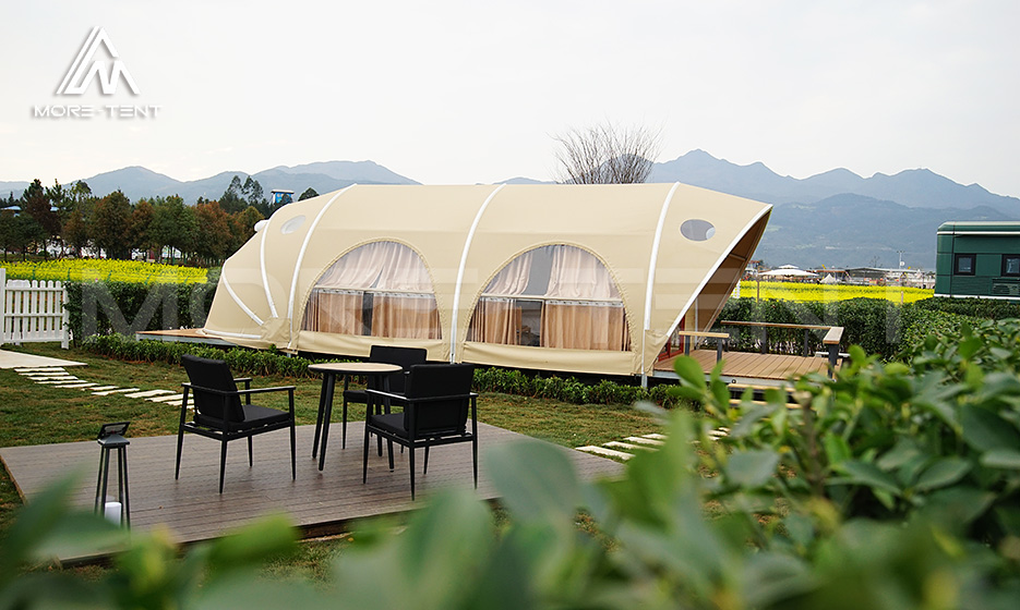 Shell glamping tent with arched windows beside a rural field