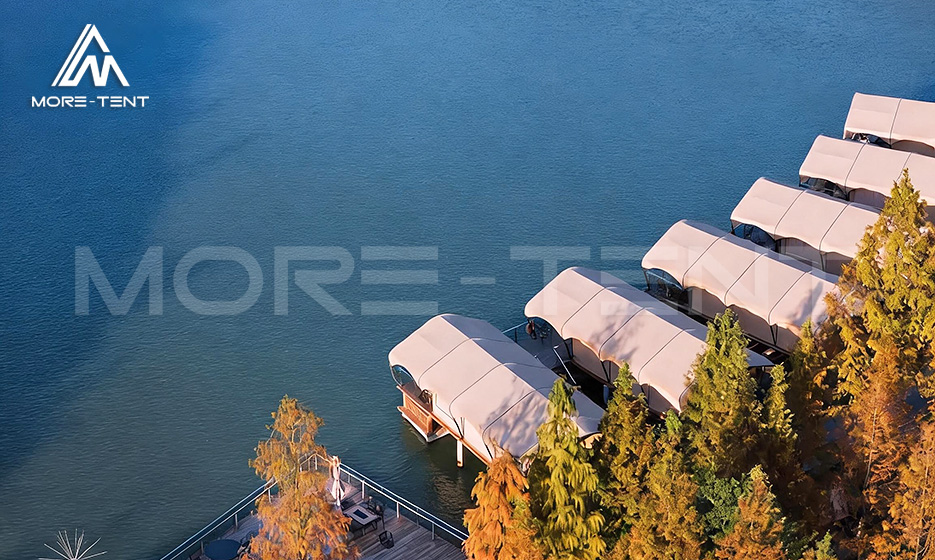 Aerial view of waterfront glamping tents lined along a blue lake