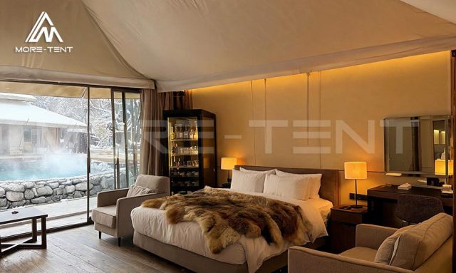 Glamping bedroom with armchairs and glass doors overlooking hot springs